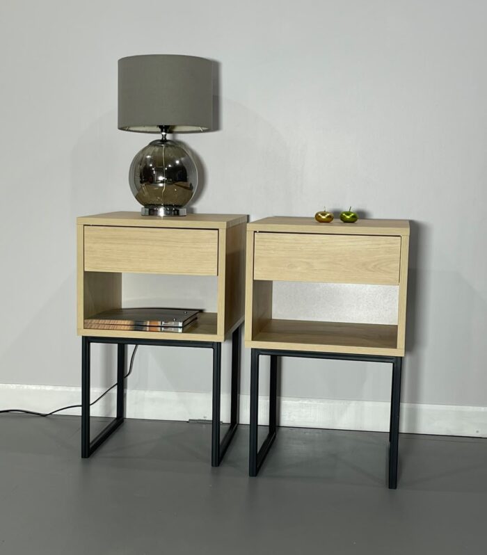 Mesa de noche industrial con estructura metálica negra, gaveta de almacenamiento y acabado en madera natural, ideal para dormitorios modernos y contemporáneos.